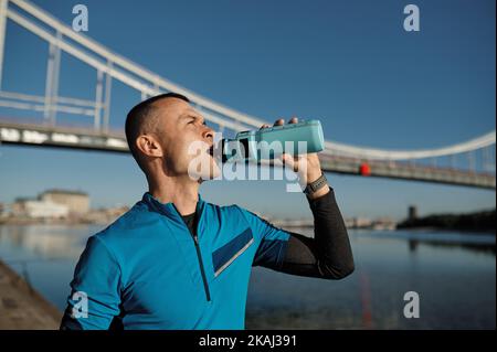 Porträt eines athletischen Mannes mittleren Alters, der eine Wasserflasche hält, um sich zu erfrischen Stockfoto