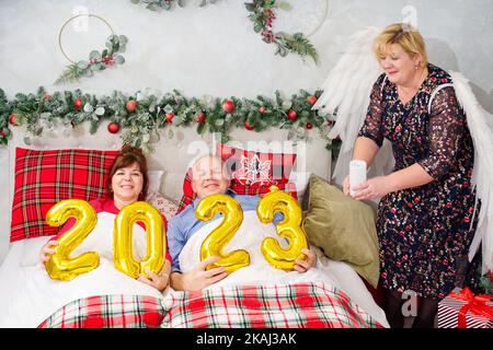 Schönes Paar liegt im Bett und plant, ein Baby zu haben. Weihnachten und frohe Neujahr mit den Zahlen 2023 Stockfoto