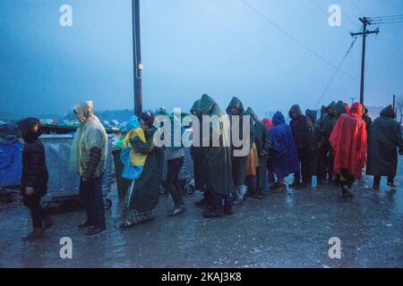 Migranten stehen am 11. März 2016 in einem provisorischen Lager an der griechisch-mazedonischen Grenze in der Nähe des griechischen Dorfes Idomeni unter dem Regen, wo Tausende von Flüchtlingen und Migranten durch die Balkangrenzblockade gestrandet sind. Der Hauptwanderweg von Griechenland nach Nordeuropa wurde am 9. März blockiert, nachdem die westlichen Balkanstaaten ihre Grenzen zugeschlagen, den Druck auf ein Abkommen zwischen der EU und der Türkei erhöht und die düstere Lage an der mazedonischen Grenze verschärft hatten. Mehr als 14.000 überwiegend syrische und irakische Flüchtlinge campen am nördlichen Grenzübergang Idomeni zu Mazedonien -- viele von ihnen seit Wochen -- Stockfoto