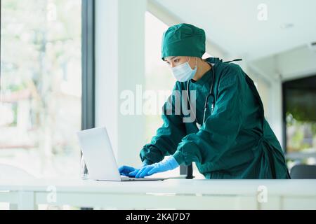 Asiatischer Arzt, der mit einem Computer Patientendaten betrachtet. Stockfoto