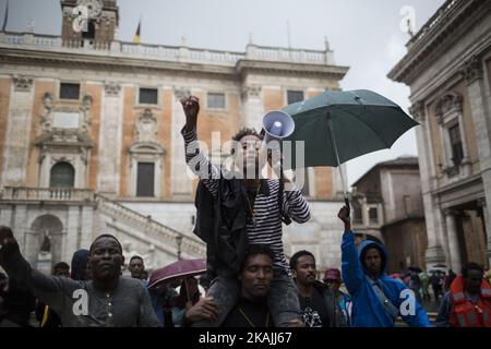 Junge Migranten rufen bei starkem Regen am 11. Oktober 2016 bei einer Demonstration auf dem Campidoglio-Platz auf dem Kapitolinischen Hügel im Zentrum Roms Parolen. Migranten und Freiwillige von "Baobab Experience" fragten nach einem sicheren Ort, an dem Flüchtlinge, hauptsächlich aus dem Horn von Afrika, untergebracht werden könnten.das Baobab-Zentrum wurde im Dezember 2015 von der Polizei nach den Anschlägen von Paris geschlossen. Doch die Baobab-Freiwilligen haben schnell ein Lager auf der Straße vor dem alten Tierheim mit Zelten und chemischen Toiletten eingerichtet, das drei Mahlzeiten am Tag serviert. (Foto von Christian Minelli/NurPhoto) *** Bitte nutzen Sie die Gutschrift von Cre Stockfoto