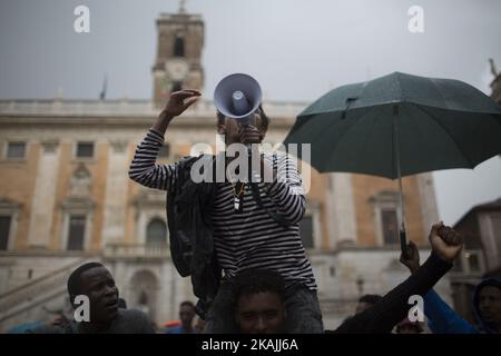 Junge Migranten rufen bei starkem Regen am 11. Oktober 2016 bei einer Demonstration auf dem Campidoglio-Platz auf dem Kapitolinischen Hügel im Zentrum Roms Parolen. Migranten und Freiwillige von "Baobab Experience" fragten nach einem sicheren Ort, an dem Flüchtlinge, hauptsächlich aus dem Horn von Afrika, untergebracht werden könnten.das Baobab-Zentrum wurde im Dezember 2015 von der Polizei nach den Anschlägen von Paris geschlossen. Doch die Baobab-Freiwilligen haben schnell ein Lager auf der Straße vor dem alten Tierheim mit Zelten und chemischen Toiletten eingerichtet, das drei Mahlzeiten am Tag serviert. (Foto von Christian Minelli/NurPhoto) *** Bitte nutzen Sie die Gutschrift von Cre Stockfoto