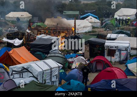 Ein Polizeibeamter sichert den Eingang zu einer brennenden Hütte im Dschungel von Calais. Riesige Brände zerstörten heute einen Hauptteil des Flüchtlingslagers. (Foto von Markus Heine/NurPhoto) *** Bitte nutzen Sie die Gutschrift aus dem Kreditfeld *** Stockfoto