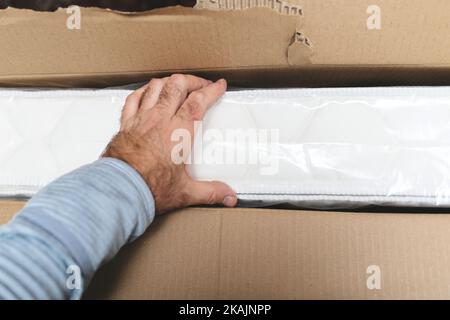 POV männliche Hand halten Entfernen aus dem Paket Unboxing Luxus Premium-Qualität Matratze für das Schlafzimmer Stockfoto