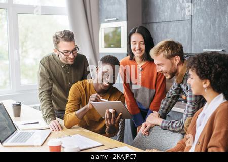 Glückliche, multirassische Mitarbeiter haben Spaß daran, bei einem Büromeeting zusammenzuarbeiten. Stockfoto