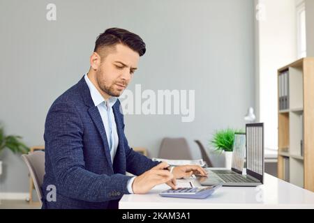 Der Finanzbuchhalter sitzt an seinem Schreibtisch und benutzt einen Rechner und einen Laptop Stockfoto