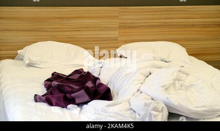 Das Bett war mit Kissen und einer gekrümmten Decke ausgestattet. Zerbröckelte Decke und Kissen auf leerem, zerknittertem Bett im Hotelzimmer nach dem Schlafen in der Nacht. Stockfoto