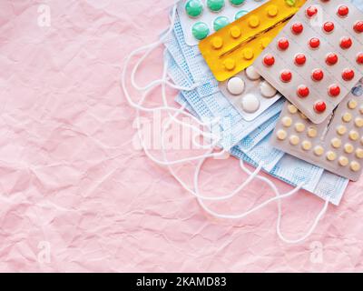 Draufsicht auf eine Packung blauer Schutzmasken und verschiedener Pillen. Coronavirus COVID-19 Konzept auf rosa zerknittertem Hintergrund mit Kopierraum. Stockfoto