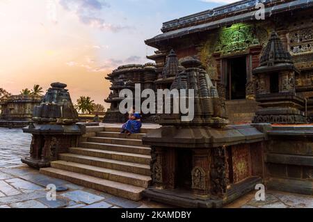 Belur, Karnataka, Indien : Channakeshava Tempel des 12.. Jahrhunderts bei Sonnenuntergang. Eine Frau sitzt auf den Stufen des Haupttempels von Kesava. Stockfoto