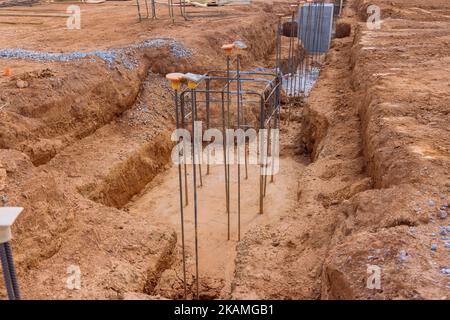 Die Bewehrung mit Stahlstäben wird in den Graben für das Betonfundament auf der Baustelle gesteckt Stockfoto