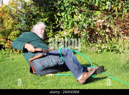 Älterer Mann im Garten und hatte einen Unfall. Umgefallen. Unfall. Scharfe Schere in der Hand. Alter Mann verletzt. Stockfoto