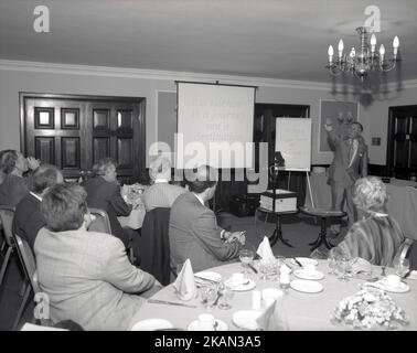 1980s, historisch, in einem Hotelzimmer, männlicher Trainer, Moderator, mit Whiteboard im Zimmer des Unternehmens, das eine Präsentation für leitende Mitarbeiter, England, Großbritannien, vorstellt. Sätze wie „ Exzellenz ist eine Reise, oder eine Desintation“ und „Change managen oder von IT gemanagt werden!“. Der Overheadprojektor oder OHP, wie er genannt wurde, war in dieser Zeit vor der Einführung des Diaprojektors und der Erstellung von „Audio-visuellen Diashows“ ein Standardinstrument für die Präsentation. Stockfoto