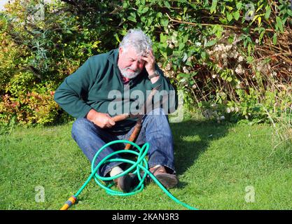 Älterer Mann im Garten und hatte einen Unfall. Umgefallen. Unfall. Scharfe Schere in der Hand. Alter Mann verletzt. Stockfoto