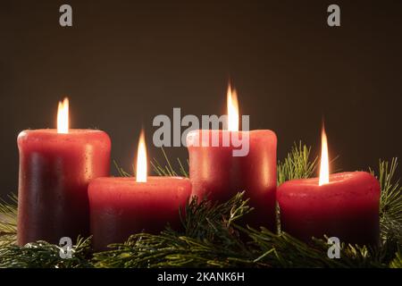 Adventskranz mit vier roten Kerzen in einem dunklen Raum mit Kopierraum angezündet und glüht Stockfoto