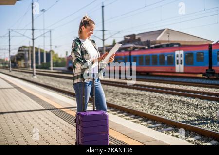 Glückliche Frau, die ein digitales Tablet auf einem Bahnhof verwendet. Stockfoto