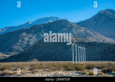 Palm Springs, Kalifornien- Windturbinen in einer Wüste am Berghang. Reihe von Windmühlen auf einer trockenen Wüste Shrobland gegen die Berge im Hintergrund. Stockfoto