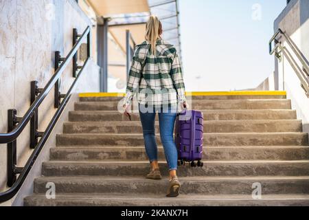 Frau mit Koffer und Ticket, die im Bahnhof über eine Treppe hinaufsteigt. Stockfoto