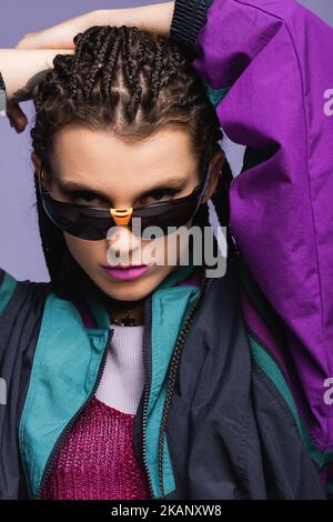 Porträt von stilvollen jungen Modell in Retro-Sonnenbrille Blick auf Kamera isoliert auf lila, Stock Bild Stockfoto