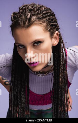 Porträt der trendigen Frau mit Dreadlocks und Make-up Blick auf Kamera isoliert auf lila, Stock Bild Stockfoto