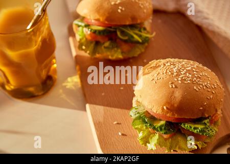 Gesunde Alternative des klassischen amerikanischen Hamburgers - Fischburger mit geräuchertem Lachs, Gurken, Tomaten und Salat unter harten Schatten. Stockfoto