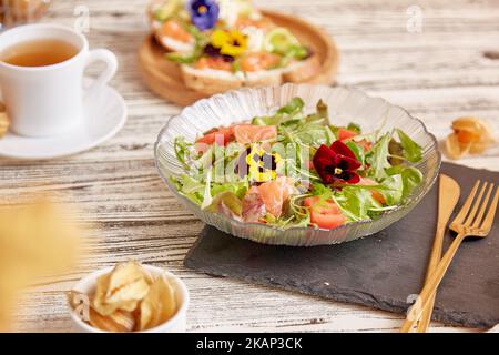 Frischer mediterraner Pescetarian-Salat mit Lachs, Gemüse, Gemüse und essbaren Blumen. Tasse Tee und Vorspeisen Stockfoto