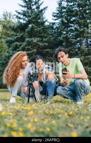 Teenager-Blogger sitzen im Sommerpark und wählen trendige Tanz-Video für Social-Media-Netzwerke Blog. Video-Live-Streaming. Multirassisches Team. Kreativ Stockfoto