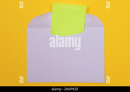 Violetter Umschlag mit leerem grünen Blatt Papier innen, auf gelbem Hintergrund liegend - Mock Up with Copy Space. Posteingang oder Benachrichtigung, Postkarte senden - Draufsicht, Flat Lay Stockfoto