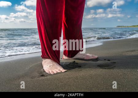 Die Füße des Weihnachtsmannes ohne Stiefel in roten Hosen an einem Sandstrand am Meer mit Kopierfläche Stockfoto