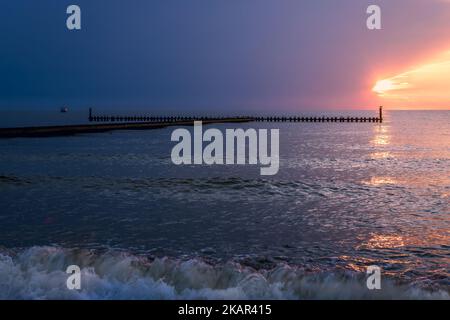 Wunderschöner Sonnenuntergang und drohender Sturm. Ein Fischerboot und Kisten auf dem Wellenbrecher im Hintergrund Stockfoto