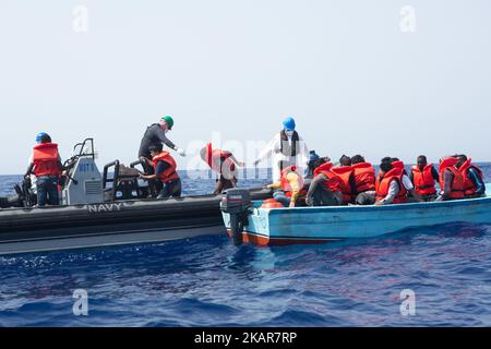 LAMPEDUSA, ITALIEN - SEPTEMBER 02: Flüchtlinge und Migranten werden gesehen, wie sie von einem überfüllten kleinen Holzboot zu einem irischen Kriegsschiff gebracht werden, nachdem sie von Such- und Rettungscrew-Mitgliedern der deutschen NGO Sea-Eye am 2. September 2017 von 46 Seemeilen (nm) mit Rettungswesten unterstützt und vorbereitet wurden. Die Sicherheitslage für SAR-NGOs wie Sey-Eye hat sich verschlechtert, nachdem die so genannte libysche Kostengarde ihr Such- und Rettungsgebiet von 12nm auf 72nm erweitert hat. Gleichzeitig ist die Zahl der geretteten Menschen aus der Not der NGOs zurückgegangen Stockfoto