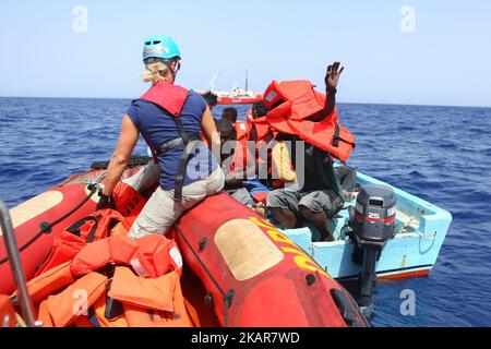 LAMPEDUSA, ITALIEN - 02. SEPTEMBER: Ein Besatzungsmitglied der deutschen Such- und Rettungsorganisation Sea-Eye verteilt am 2. September 2017 Rettungswesten an Flüchtlinge und Migranten, die in einem überfüllten Holzboot etwa 46 Seemeilen (nm) in libysch eingeweihten Gebiet warten. Die Sicherheitslage für SAR-NGOs wie Sey-Eye hat sich verschlechtert, nachdem die so genannte libysche Kostengarde ihr Such- und Rettungsgebiet von 12nm auf 72nm erweitert hat. Gleichzeitig wurde die Zahl der geretteten Menschen aus der Not von NGOs aufgrund dieser Tatsache abgelehnt. (Bild:Christian Marquardt) (Foto von Chris Stockfoto