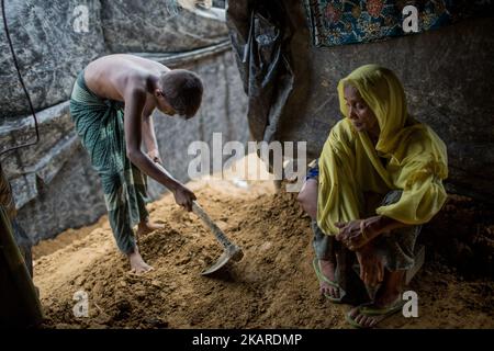 Ein Rohingya-Junge schneidet Boden, um den Boden in ihrem provisorischen Tierheim vorzubereiten, und ihre Enkelmutter sitzt neben ihm. Flüchtlingslager Balukhali, Cox’s Bazar, Chittagong, Bangladesch. 23. September 2017. Seit Ende August sind rund 430.000 Rohingya vor der Gewalt im Bundesstaat Rakhine in Myanmar geflohen. (Foto von Turjoy Chowdhury/NurPhoto) Stockfoto