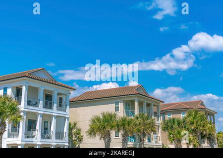 Destin, Florida- Strandhäuser mit Balkonen und Palmen an der Vorderseite. Fassade von dreistöckigen Häusern vor dem Hintergrund des klaren Himmels. Stockfoto