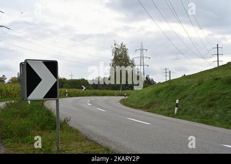 Warnung schwarz-weißer Pfeil Verkehrsschild auf scharfe, gefährliche Kurve in einer bergigen Gegend. Stockfoto