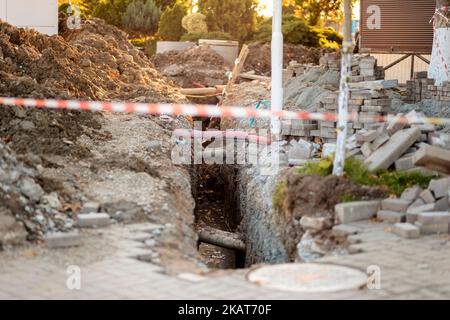 Reparatur der Kanalisation auf der Straße. Ausgegraben, gestapelt Tische und Müll. Bereich der Bauarbeiten Zaun mit Klebeband. Industrielle und städtische Konstrukteure Stockfoto