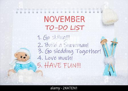 To-Do-Liste im November. Notizblock mit To-Do-Liste: Skifahren, Schneemann bauen, Rodeln, lieben, Spaß haben und ein Spielzeug Teddybär in blauer Kleidung, blaue Ski, Stockfoto