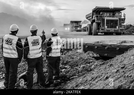 Große Dump Trucks transportieren Platinerz zur Verarbeitung mit Bergbau-Sicherheitsinspektoren im Vordergrund Stockfoto