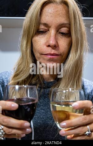 Junge blonde Frau mit zwei Kristallgläsern mit Rot- und Weißwein. Konzept des Alkoholismus bei Frauen. Stockfoto