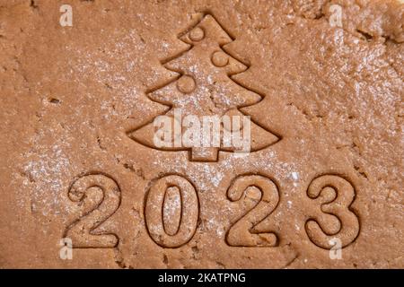 Aus Lebkuchenteig werden die Zahlen des Jahres 2023 und der Weihnachtsbaum ausgeschnitten. Wir kochen hausgemachtes Lebkuchen zu Hause. Neujahrskarte aus dem t Stockfoto