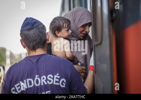 (9/14/2015) Roeszke, Ungarn. Mutter mit Baby, das in den Zug steigen und von einem Polizisten beobachtet wird. Ungarn war ein großes Transitland für Migranten, von denen viele nach Österreich und Deutschland weiterreisen wollen.2015 errichtete Ungarn an seiner Grenze zu Serbien und Kroatien eine Grenzbarriere. Der Zaun wurde während der europäischen Migrationskrise errichtet, um die Sicherheit der Grenzen zu gewährleisten, indem Flüchtlinge und Einwanderer daran gehindert werden, illegal einzureisen, und die Möglichkeit zur Einreise über offizielle Kontrollpunkte und zur Inanspruchnahme von Asyl in Ungarn gemäß internationalem und europäischem Recht ermöglicht wird. Die Zahl o Stockfoto