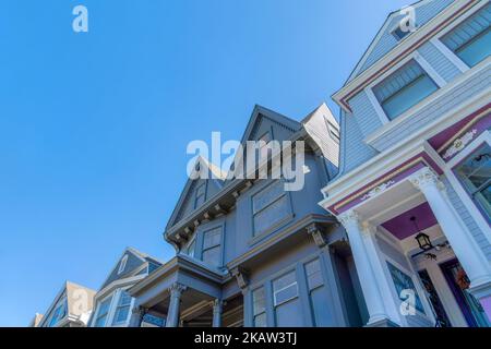 Blick auf viktorianische Häuser von unten gegen den Himmel in San Francisco, CA. Es gibt ein graues Haus auf der linken Seite mit dekorativen Vorhaussäulen und Lorbeer Stockfoto