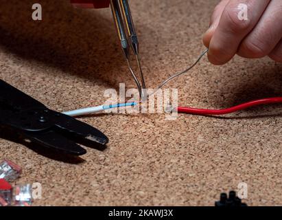 Löten - Verbindungsdrähte mit Zinn und Lötkolben, Werkstatt, im Hintergrund elektrische Elemente, Kabel Stockfoto