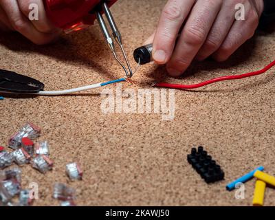 Löten - Verbindungsdrähte mit Zinn und Lötkolben, Werkstatt, im Hintergrund elektrische Elemente, Kabel Stockfoto