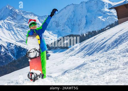 Boy in Santa Claus Hut stehen mit Snowboard über Bergen Stockfoto