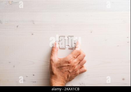 Top view of male hand placing blank puzzle piece over plain simple wooden background. Stockfoto
