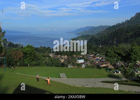 Zwei Kinder spielten mit dem Blick auf den Toba-See vor ihnen. Der Toba-See ist der größte vulkanische See in Südostasien. Der See liegt in Nord-Sumatra, Indonesien hat eine Länge von etwa 100 Kilometern, eine Breite von etwa 30 Kilometern und eine Tiefe von bis zu 505 Metern. In der Mitte dieses Sees befindet sich eine vulkanische Insel namens Samosir Island. Der Toba-See bildet sich schätzungsweise zum Zeitpunkt der Explosion vor etwa 73.000-75.000 Jahren und ist eine uralte Toba-Supervulkan-Eruption. Derzeit Lake Toba wurde zu einem der beliebtesten touristischen Destinationen der lokalen und ausländischen Touristen. (Pho Stockfoto