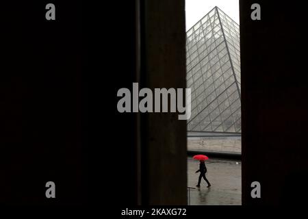 Eine Frau mit einem roten Regenschirm läuft am 9. April 2018 vor der Pyramide des Louvre in Paris, Frankreich. ( Foto von Pedro Fiuza/NurPhoto) Stockfoto