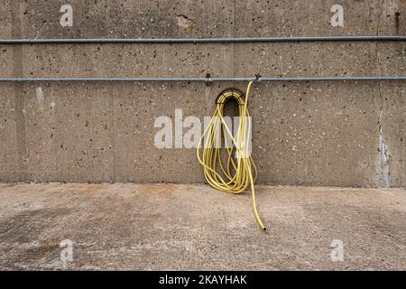 Gelber Wasserschlauch, der an einer Betonwand hängt. Stockfoto