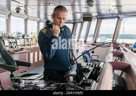 Deckoffizier bei Frachtoperationen auf der Wache. Mann in Weiß mit UKW-Funk. Gewerblicher Versand. Frachtschiff. Stockfoto