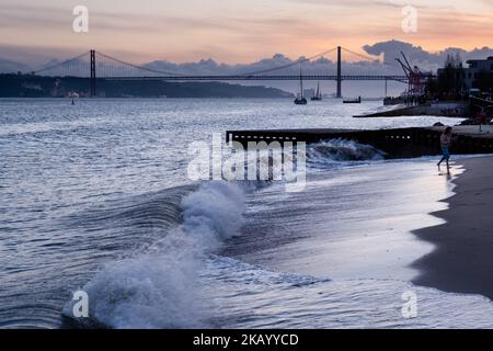 LISSABON-ABEND: Blick auf die Brücke Ponte 25 de Abril und Santuário de Cristo Rei auf der Promenade Tejo entlang des Flusses Tejo (Rio Tejo) Strand und Wellen Stockfoto